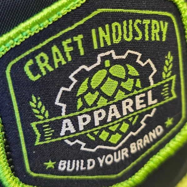 Close-up of a navy and lime green Craft Industry Apparel woven patch with a hop and gear design