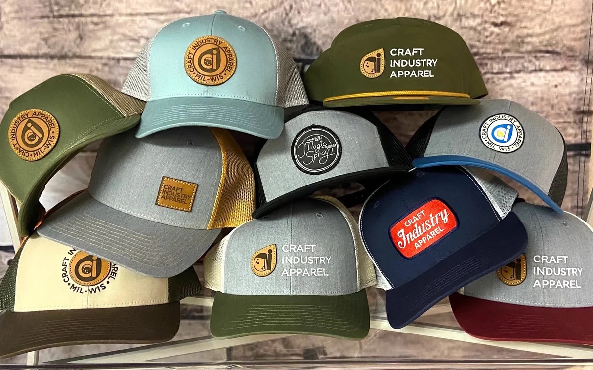 Stack of custom trucker hats with leather, woven and embroidered Craft Industry Apparel patches
